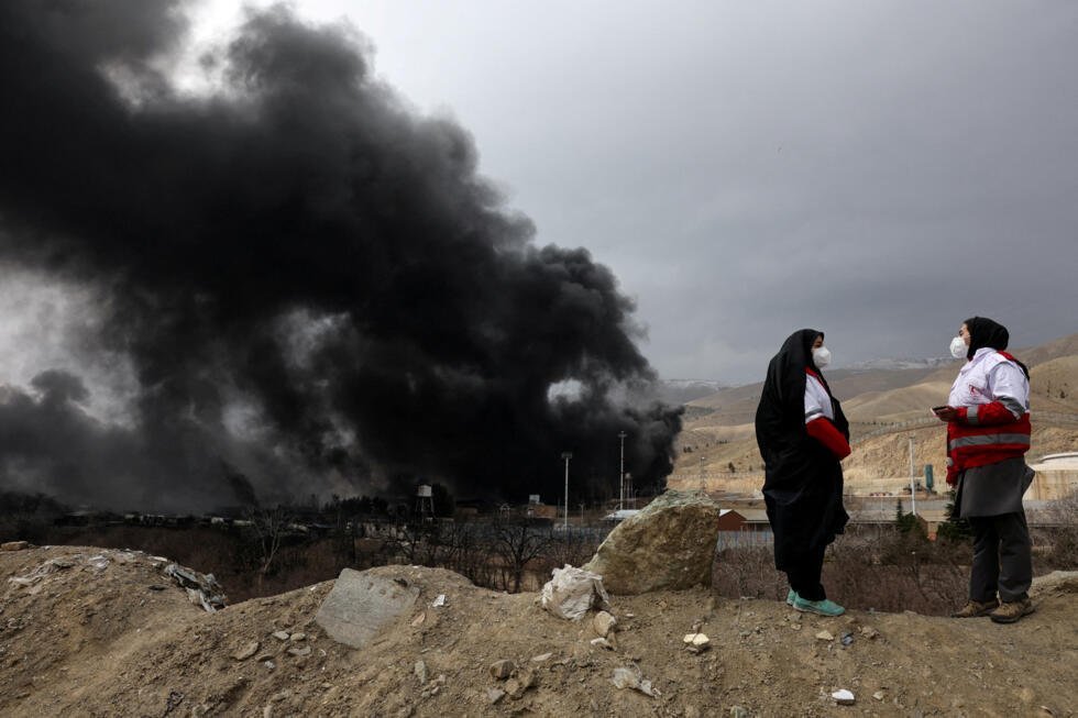 Miembros de la Media Luna Roja conversan entre sí mientras se eleva el humo tras un supuesto ataque a los tanques de combustible de Shahran, en medio del conflicto entre Estados Unidos e Israel con Irán, en Teherán, Irán, el 8 de marzo de 2026.