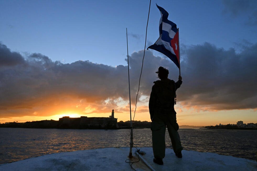 Un activista sostiene una bandera cubana en la cubierta del barco pesquero Maguro, parte de una flotilla con ayuda humanitaria para Cuba, a su entrada en el puerto de La Habana, el 24 de marzo de 2026