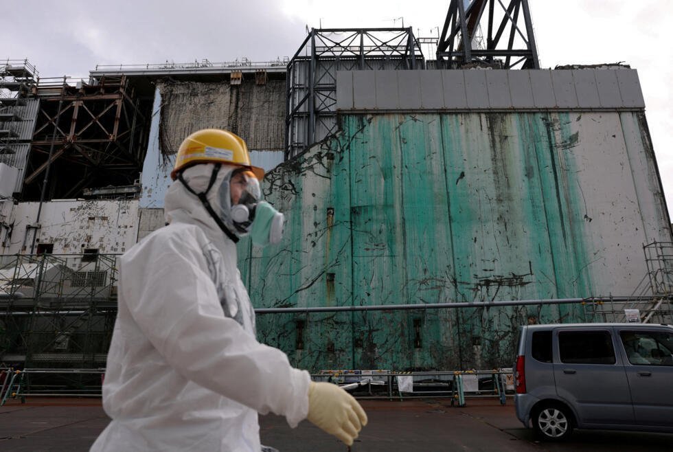 Un trabajador con traje protector y mascarilla pasa junto al reactor número 3, en la central nuclear de Fukushima (Japón), el 22 de enero de 2026.