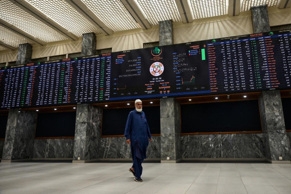 Un agente bursátil pasa frente a unos paneles electrónicos con la cotización de las acciones del Pakistan Stock Exchange, el 10 de marzo de 2026 en la ciudad paquistaní de Karachi