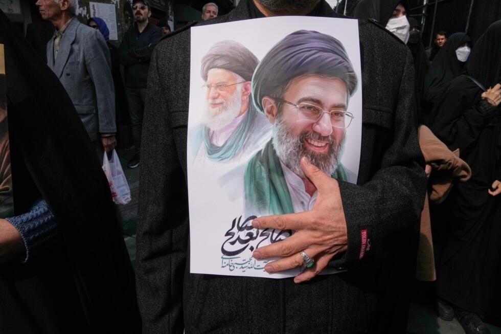 Un hombre de luto sostiene un cartel que representa al ayatolá Mojtaba Khamenei, a la derecha, sucesor de su difunto padre, el ayatolá Ali Khamenei, a la izquierda, como líder supremo, durante la procesión fúnebre de altos funcionarios militares iraníes y civiles muertos durante la campaña estadounidense-israelí en Teherán, Irán, el miércoles 11 de marzo de 2026.