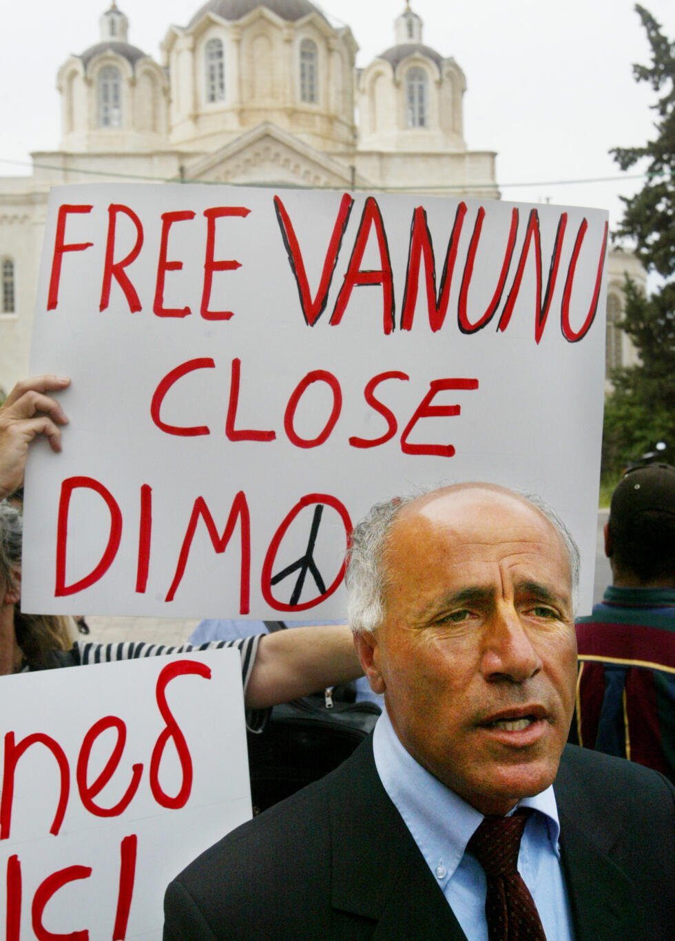 El denunciante nuclear israelí Mordechai Vanunu habla con los periodistas mientras un simpatizante sostiene un cartel a sus espaldas, a su llegada a una vista en un tribunal de Jerusalén, el martes 12 de abril de 2005.